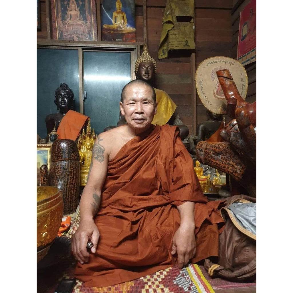 Buddhist monk seated in shrine with Buddha statues holding Phra Ngang love charm amulet for blessings