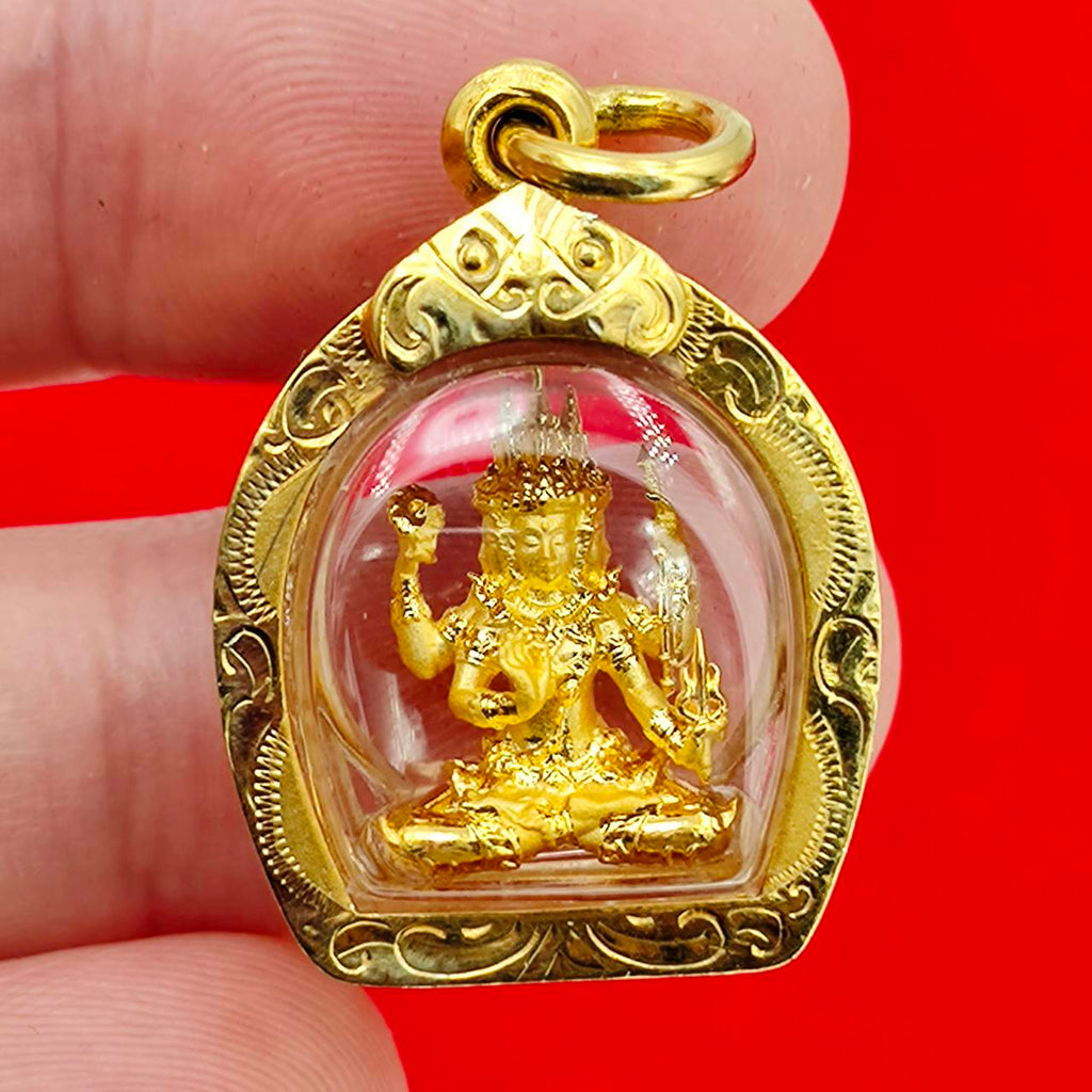 Phra Phrom amulet gold case pendant showing small seated four armed deity in clear domed gold frame on red background