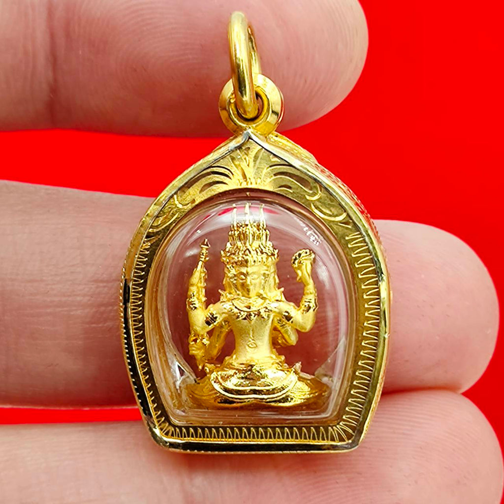 Thai Blessing Co Phra Phrom amulet gold case showing small gold Phra Phrom statue in clear domed pendant held between fingers
