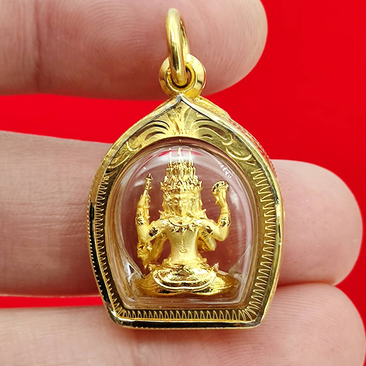 Thai Blessing Co Phra Phrom amulet gold case showing small gold Phra Phrom statue in clear domed pendant held between fingers