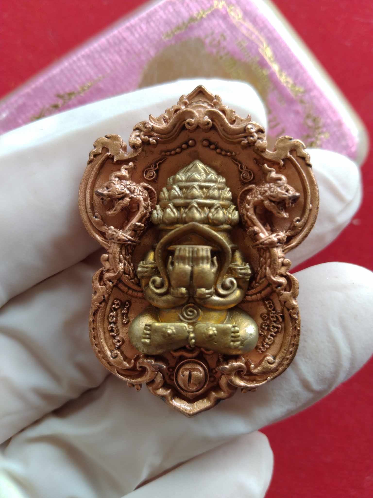 Thai Blessing Co Phra Pidta amulet for wealth ornate copper and gold pendant with intricate Naga frame held in gloved hand