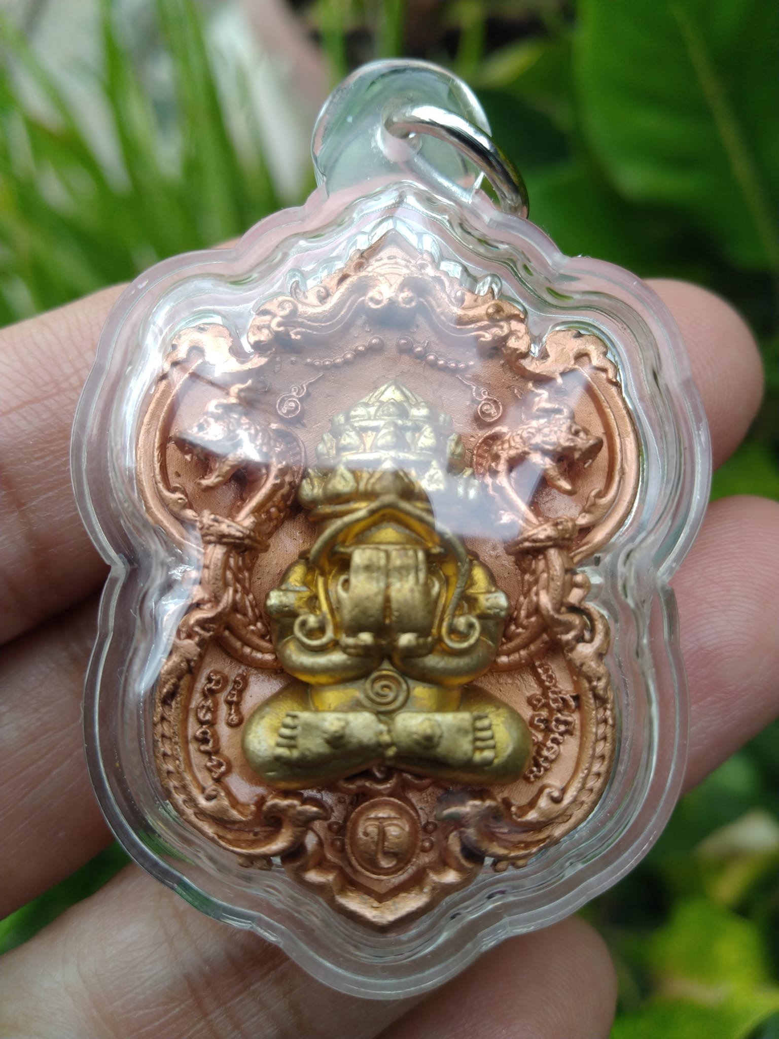 Phra Pidta amulet for wealth gold and bronze Thai pendant in clear protective casing held in hand