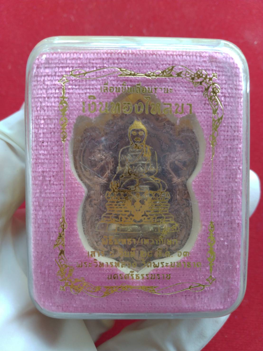 Phra Pidta amulet for wealth in clear plastic display case with pink velvet backing and gold Thai script