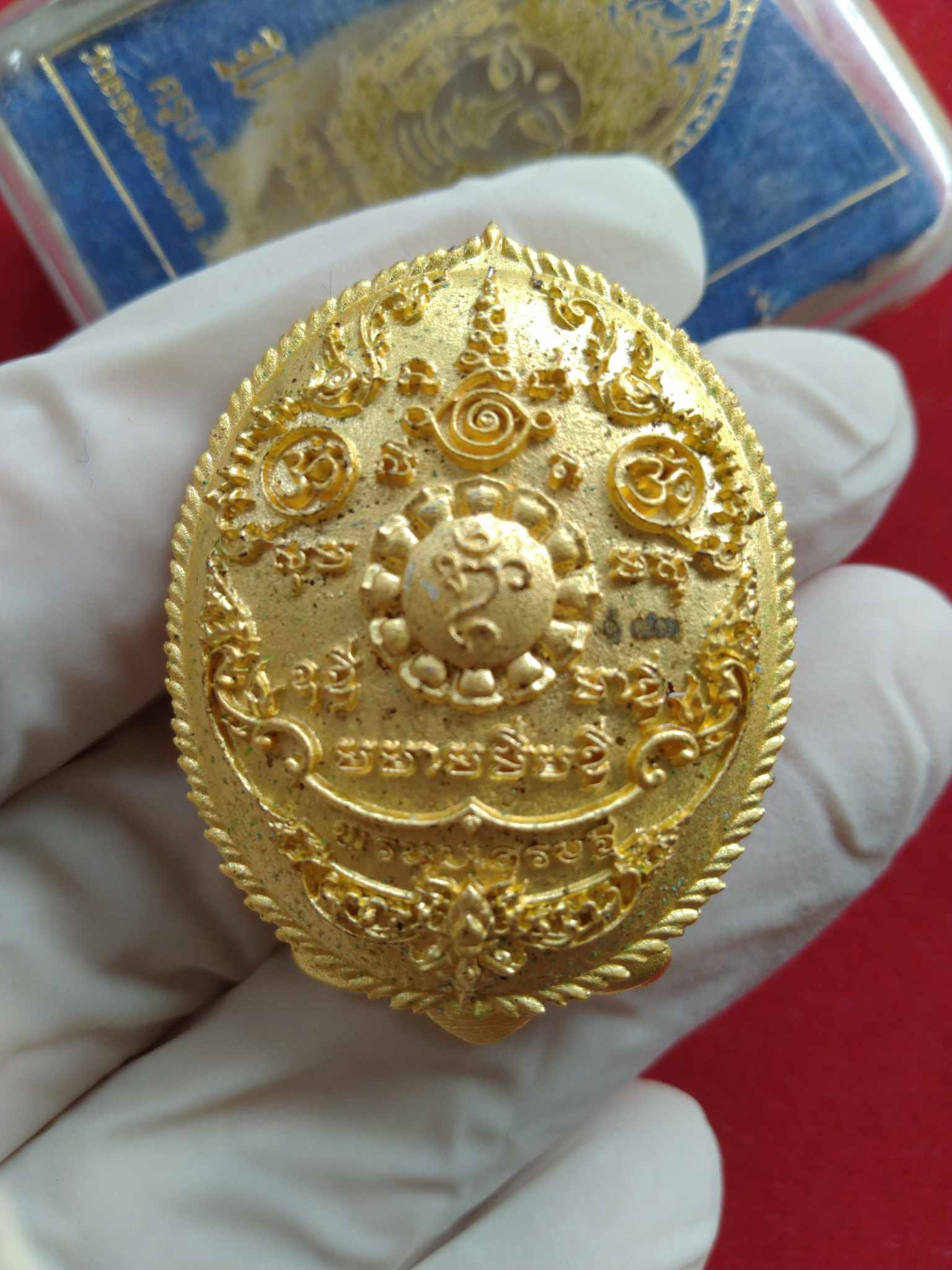 Phrom Setthi amulet for wealth gold oval Thai pendant with intricate sacred engravings held in gloved hand