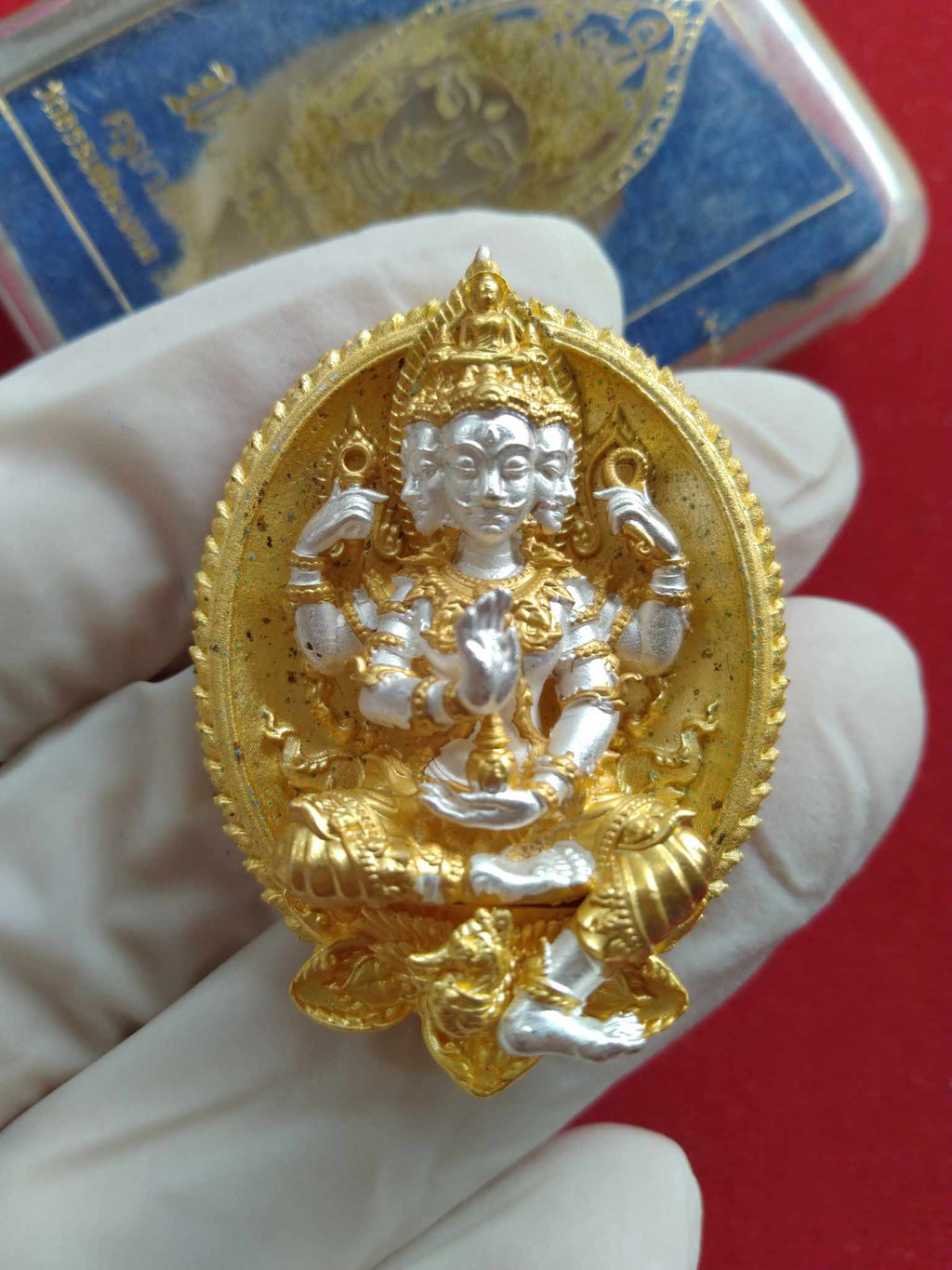 Thai Blessing Co gold and silver Phrom Setthi amulet for wealth oval pendant showing ornate four faced deity held in gloved hand
