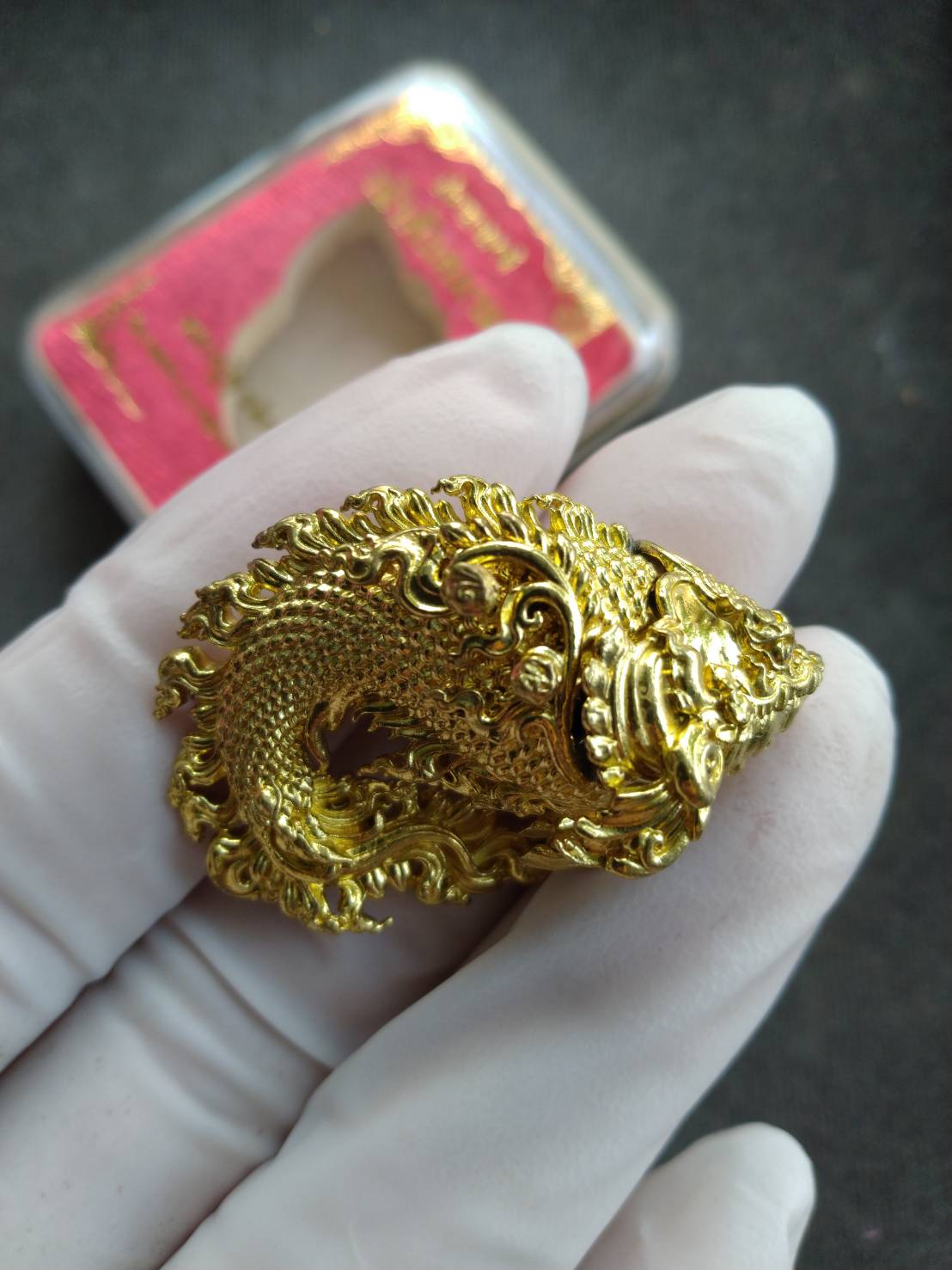 Gold ornate Pla Anon Chao Sua Siam amulet for wealth held in white glove with display box