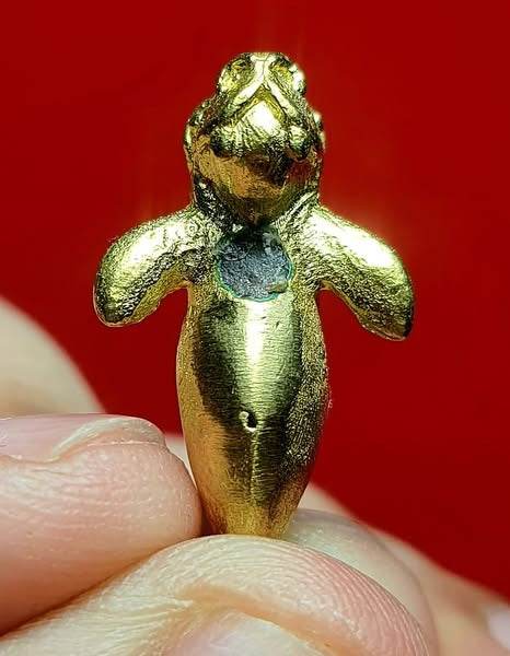 Gold Pla Du Yong (Manatee) Amulet held between fingers on red background Thai talisman