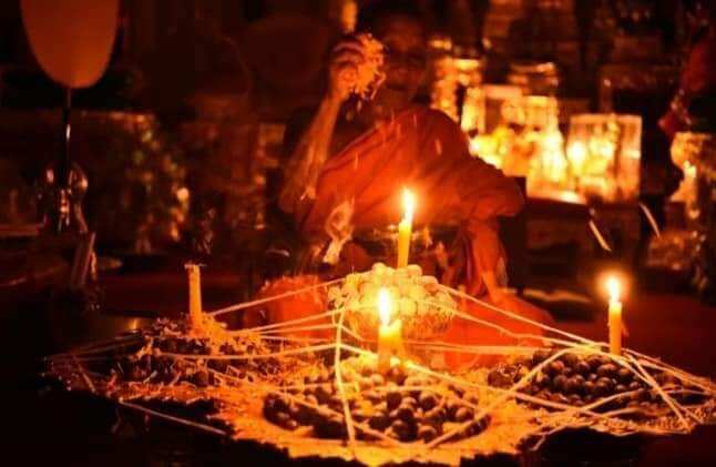 Thai monk performing blessing ritual with Rahu Garuda mercury talisman ball on candlelit tray