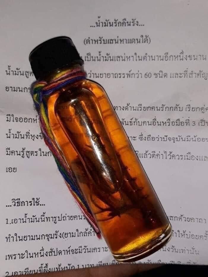 Small glass vial of amber oil with black cap and colorful cord on Thai paper rare thai attraction oil for relationships