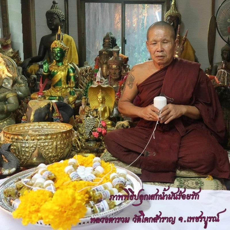 Thai monk blessing Roi Rak Luang Ta Ruam oil for attraction bottles with Buddha statues and marigold garlands