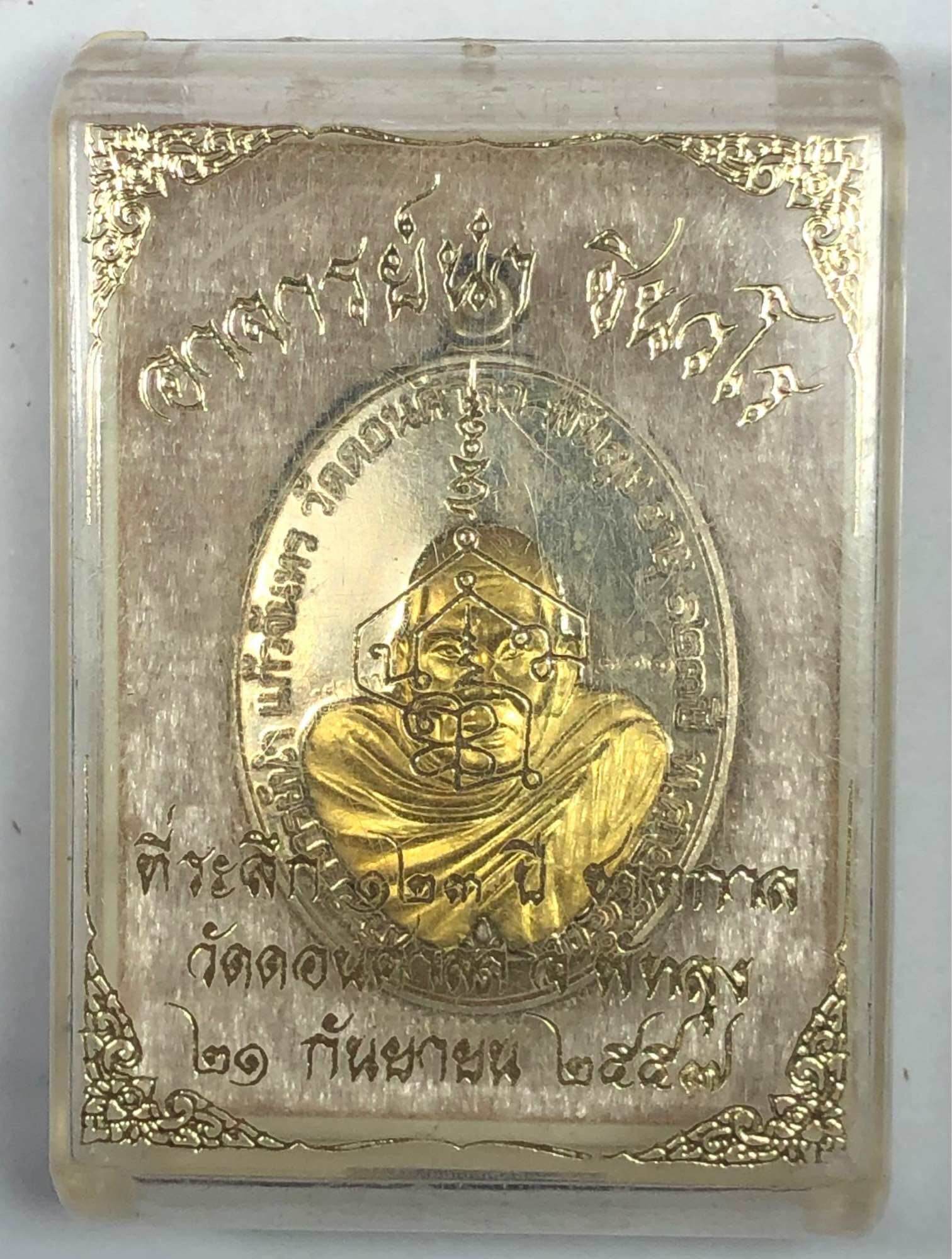 Chakkalgan Edition Thai amulet gold medallion in clear plastic case with embossed monk figure and Thai script