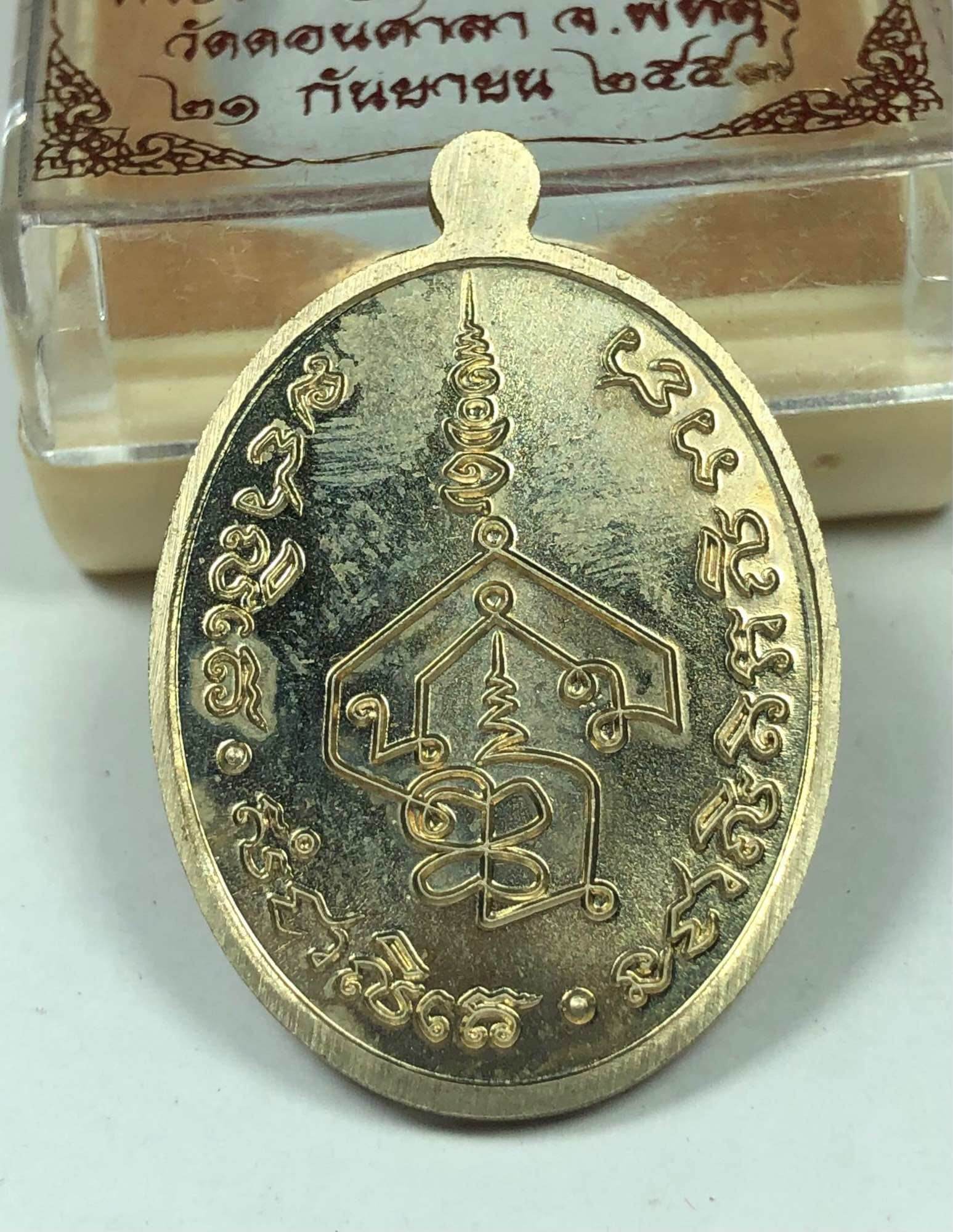 Gold oval pendant with intricate yantra symbol and engraved Thai script Chakkalgan Edition Thai amulet on clear display box
