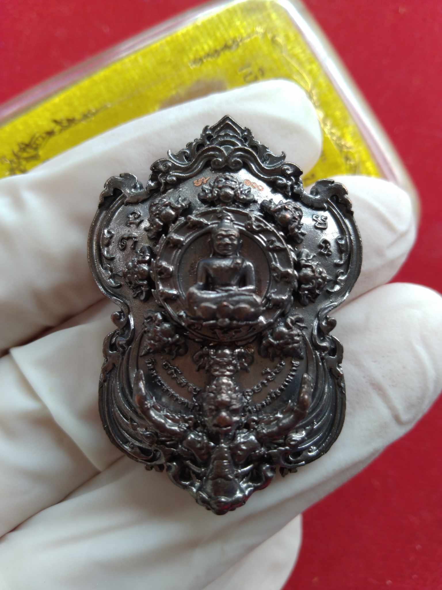 Thai Blessing Co ornate dark metal pendant showing seated Buddha held in gloved hand Si Maharaj Phangpakal rattle amulet