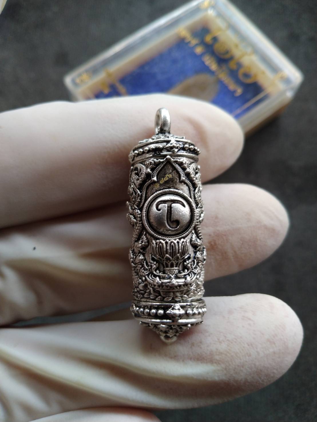 Takrud Ai Khai amulet for wealth silver engraved cylindrical pendant with intricate Thai motifs held by gloved hand