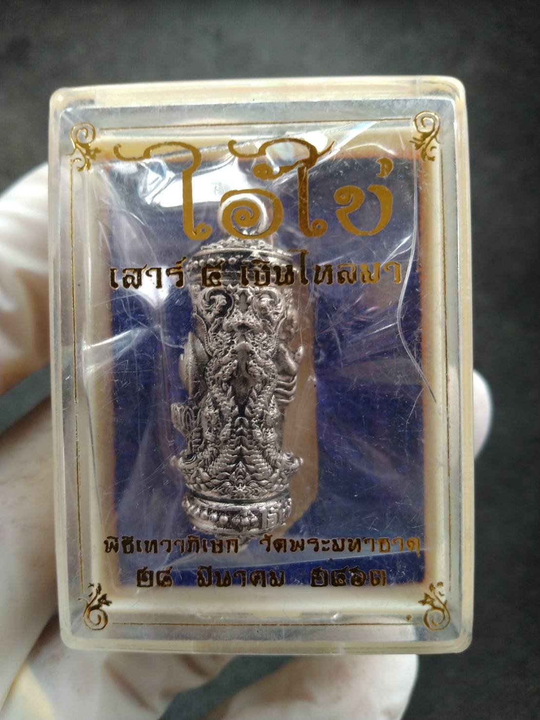 Silver Takrud cylinder amulet in clear plastic display box with Thai script Takrud Ai Khai amulet for wealth