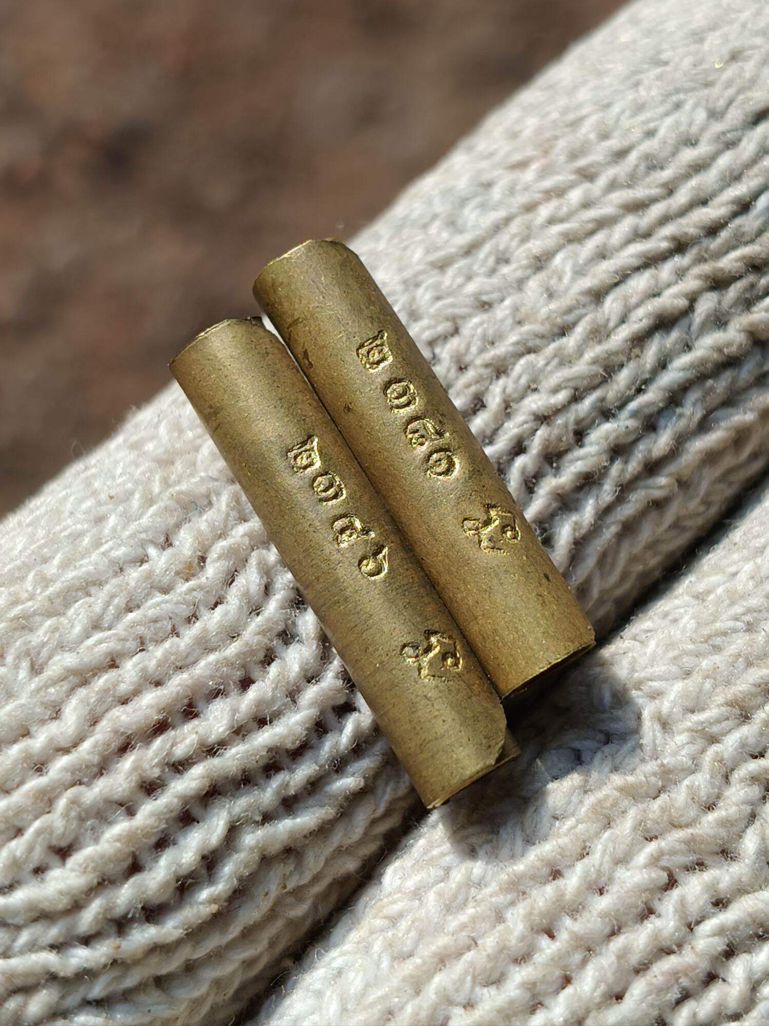 Close up two brass Takrud tubes with Thai inscriptions on knit glove Takrud amulet for protection. Thai Blessing Co