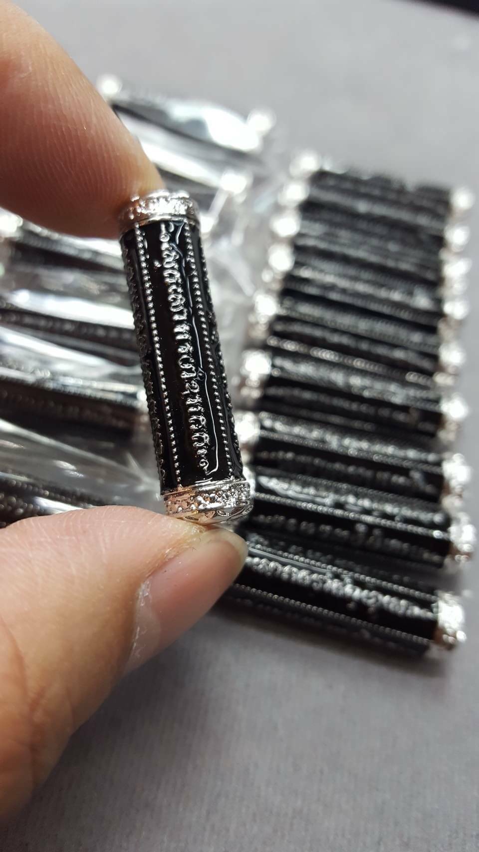 takrut 5 lines amulet silver capped black scroll with Thai script shown held between fingers multiple pieces