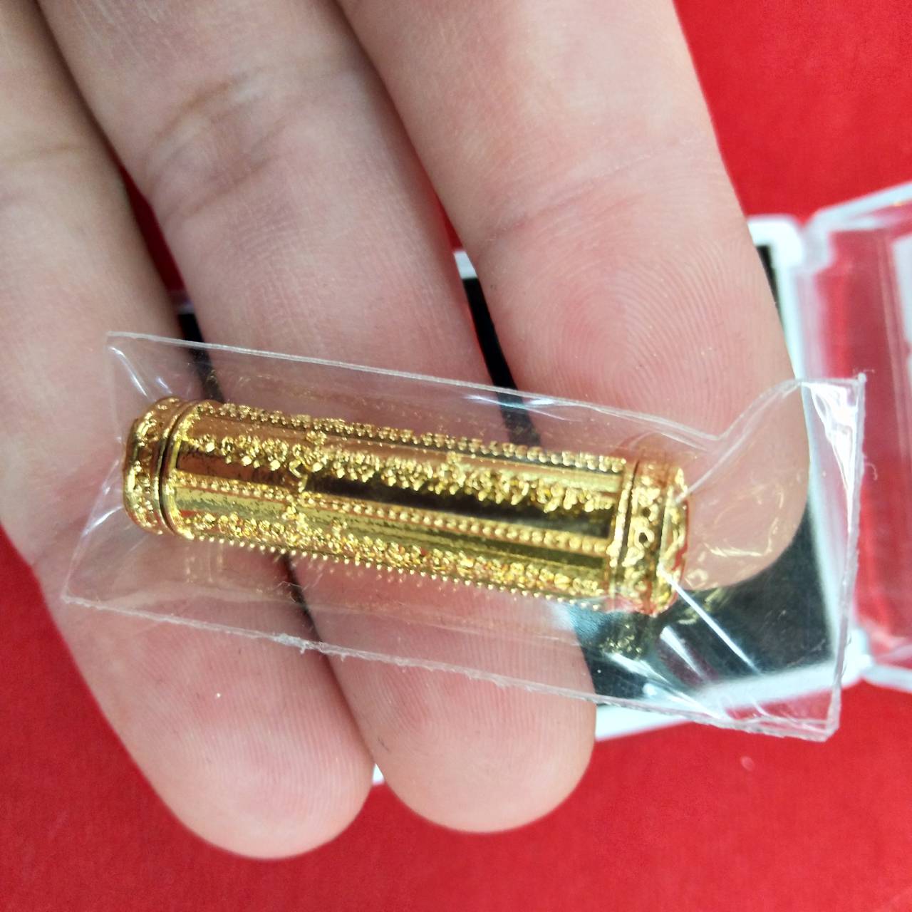 Gold engraved cylinder in plastic sleeve held by fingers takrut 5 lines amulet from Thai Blessing Co