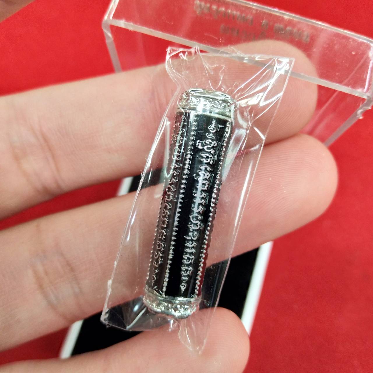 Thai Blessing Co takrut 5 lines amulet in clear plastic wrap held between fingers showing silver ends and script
