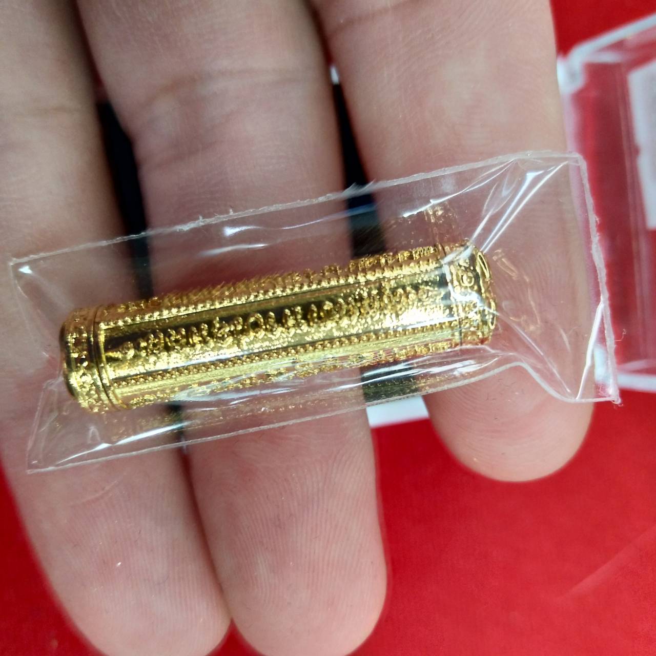 Gold takrut 5 lines amulet scroll in clear plastic pouch held between fingers by Thai Blessing Co