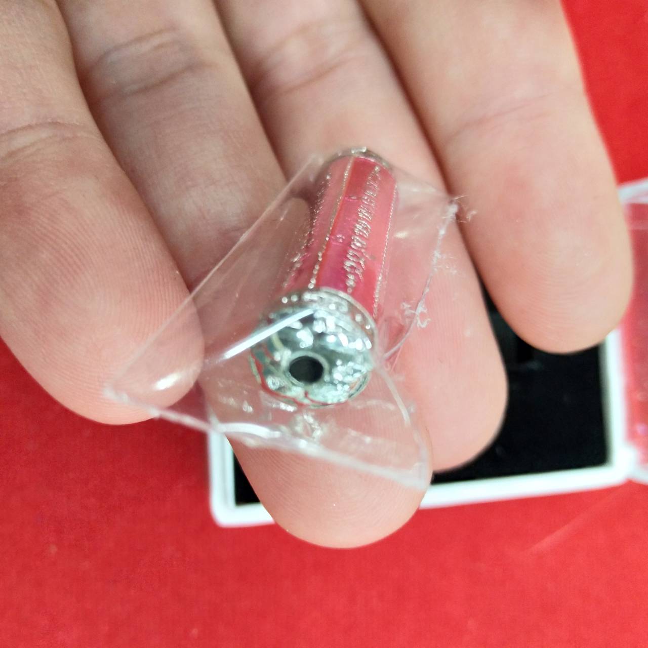 Close up of small red takrut 5 lines amulet protective talisman in silver casing wrapped in plastic held between fingers