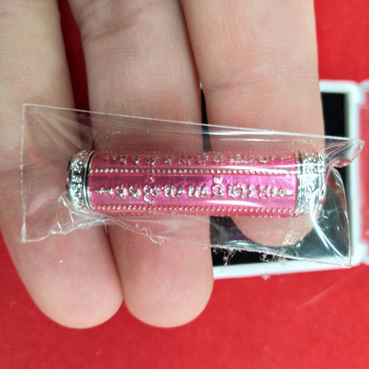 Pink metal takrut 5 lines amulet with silver caps in plastic sleeve held between fingers