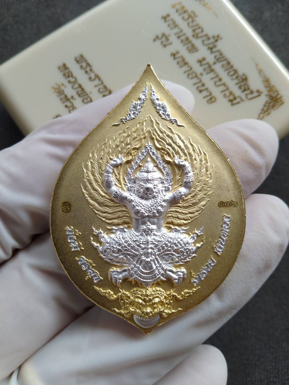 Tao Wessuwan amulet coin teardrop gold and silver two tone pendant held by gloved hand