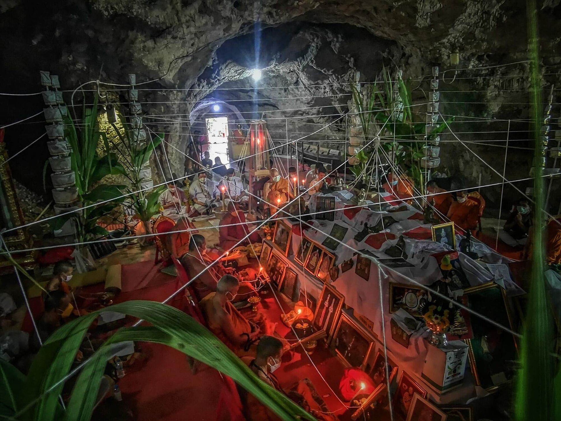 Tao Wessuwan Amulet - Vann Material, Blessed by 12 Esteemed Monks . Monks in cave temple blessing amulets with candles and threads