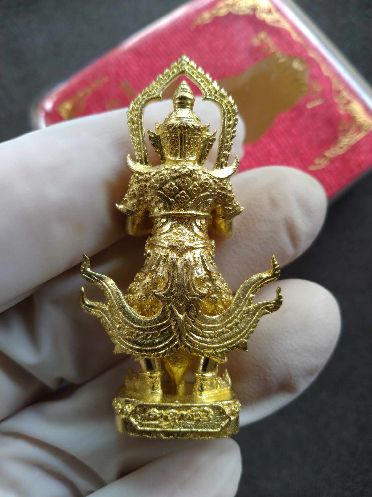 Handheld gold Thai Taow Wessuwan amulet for protection. Ornate gilt pendant with intricate details and red presentation box