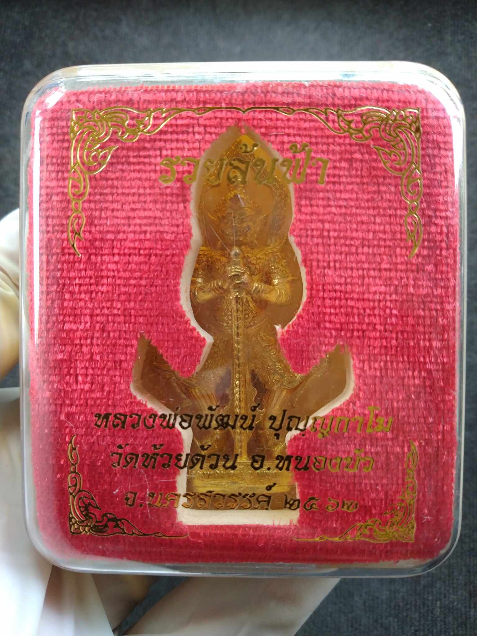 Taow Wessuwan amulet for protection. Gold metal talisman in clear plastic case on red velvet backing with Thai script