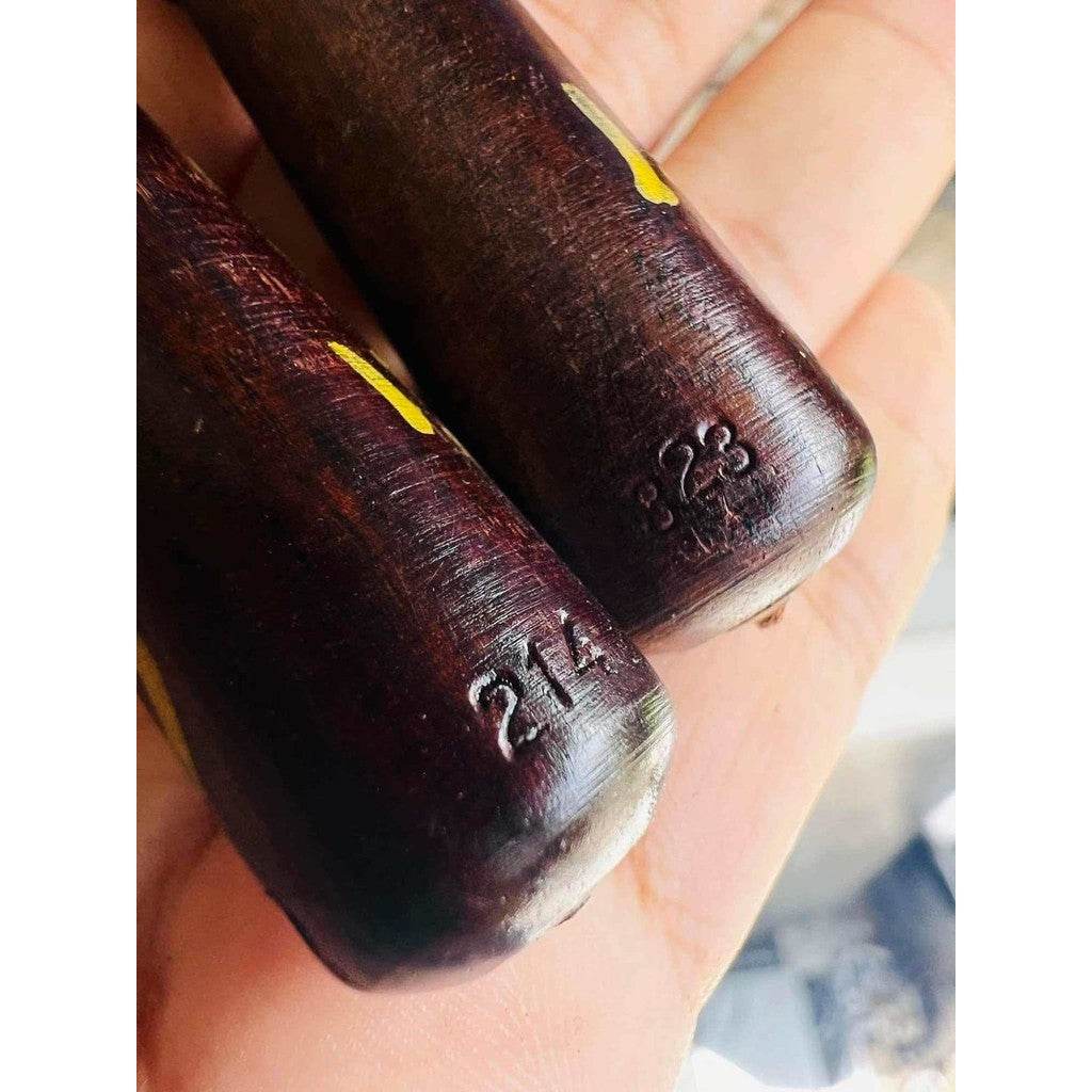 Hand holding two dark wooden amulet sticks stamped 214 and Thai script symbols Thai charm and fortune talisman