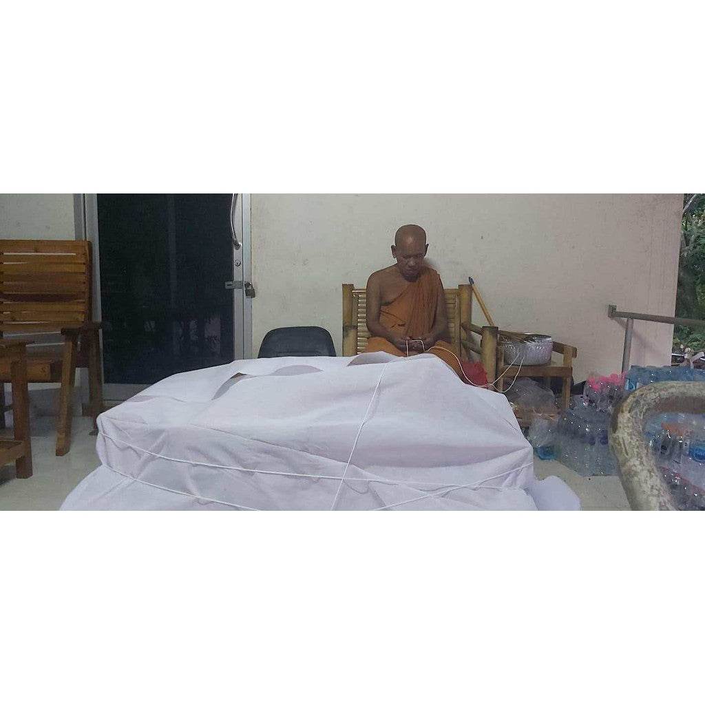 Thai charm and fortune talisman wrapped on table while a person in orange robe performs a ritual indoors