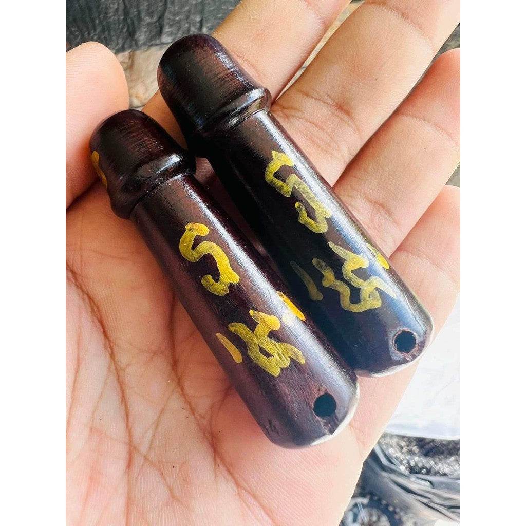 Pair of dark wooden cylinder amulets with gold script held in hand pendant beads Thai charm and fortune talisman
