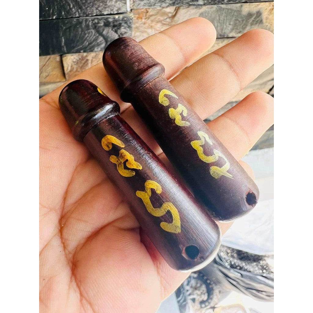 Hand holding two wooden amulets with gold script holes for cord Thai charm and fortune talisman
