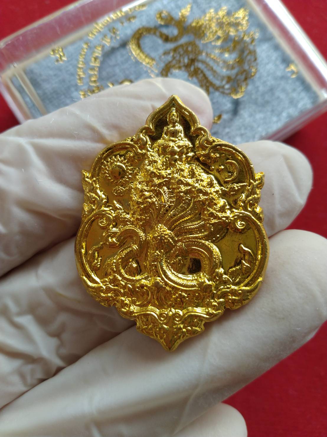 Thai fortune amulet Heart of Wealth gold ornate Naga style pendant held in gloved hand by Thai Blessing Co