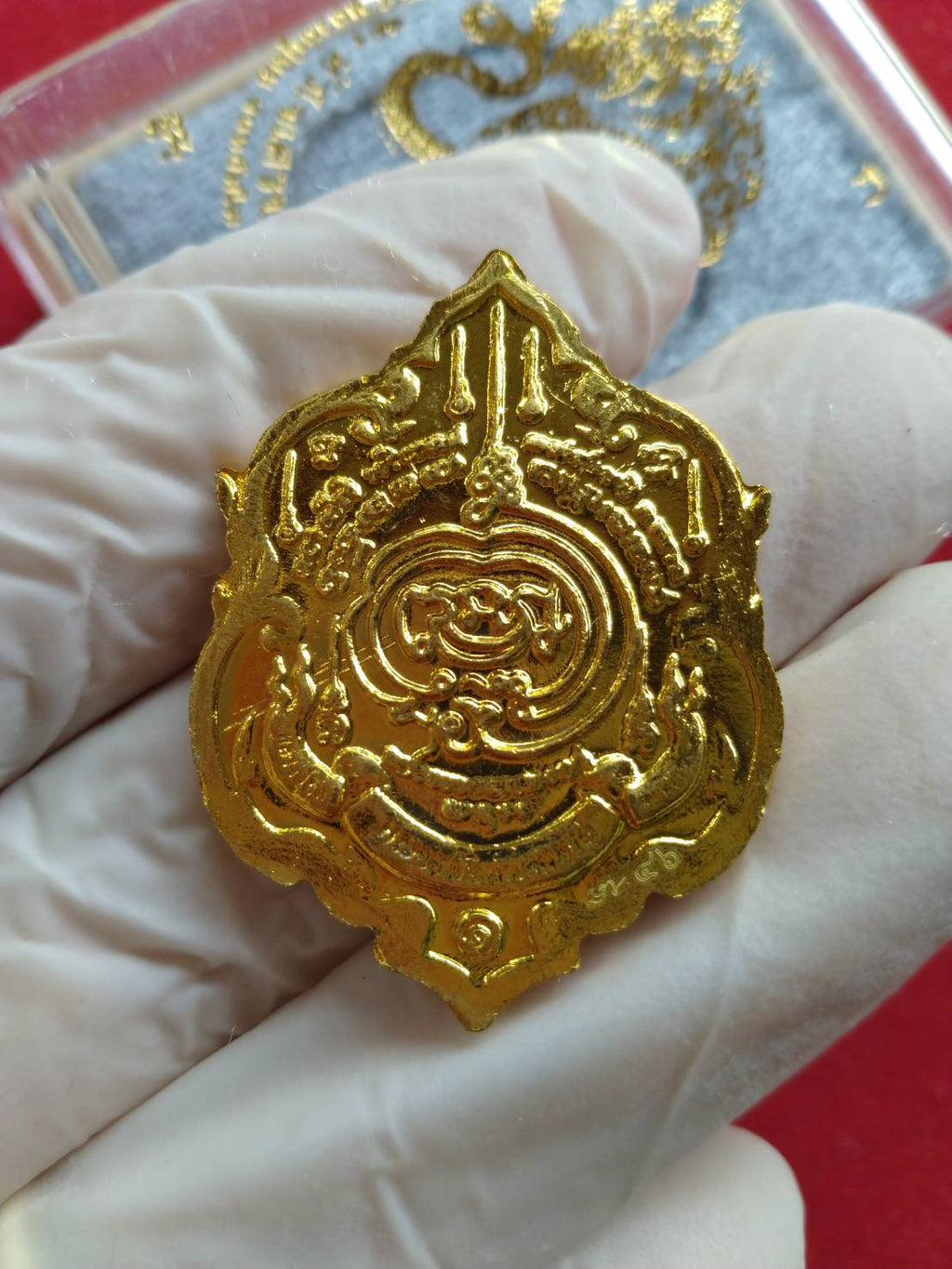 Thai fortune amulet Heart of Wealth gold pendant with intricate sacred design held in gloved hand
