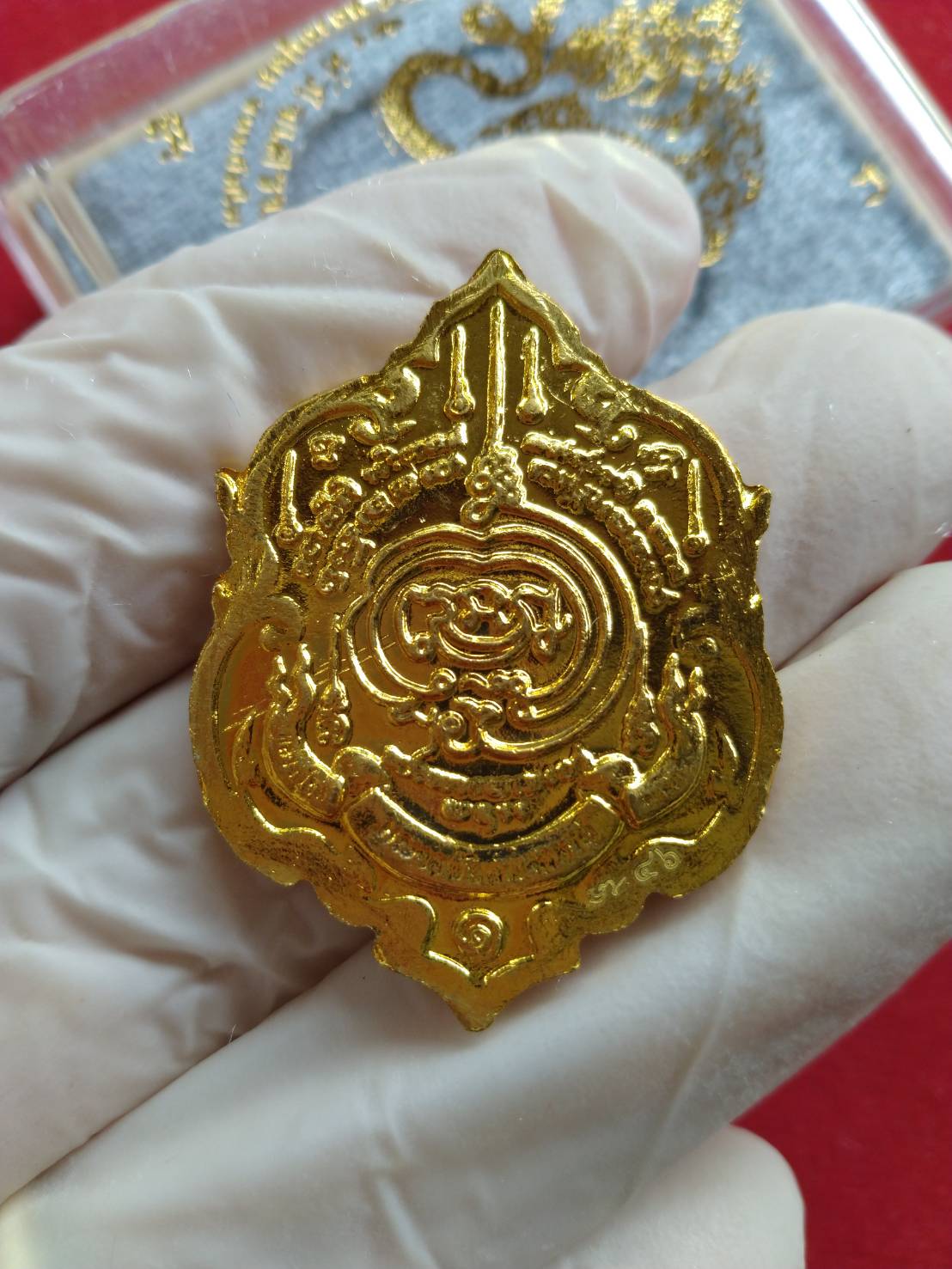 Thai fortune amulet Heart of Wealth gold pendant with intricate sacred design held in gloved hand