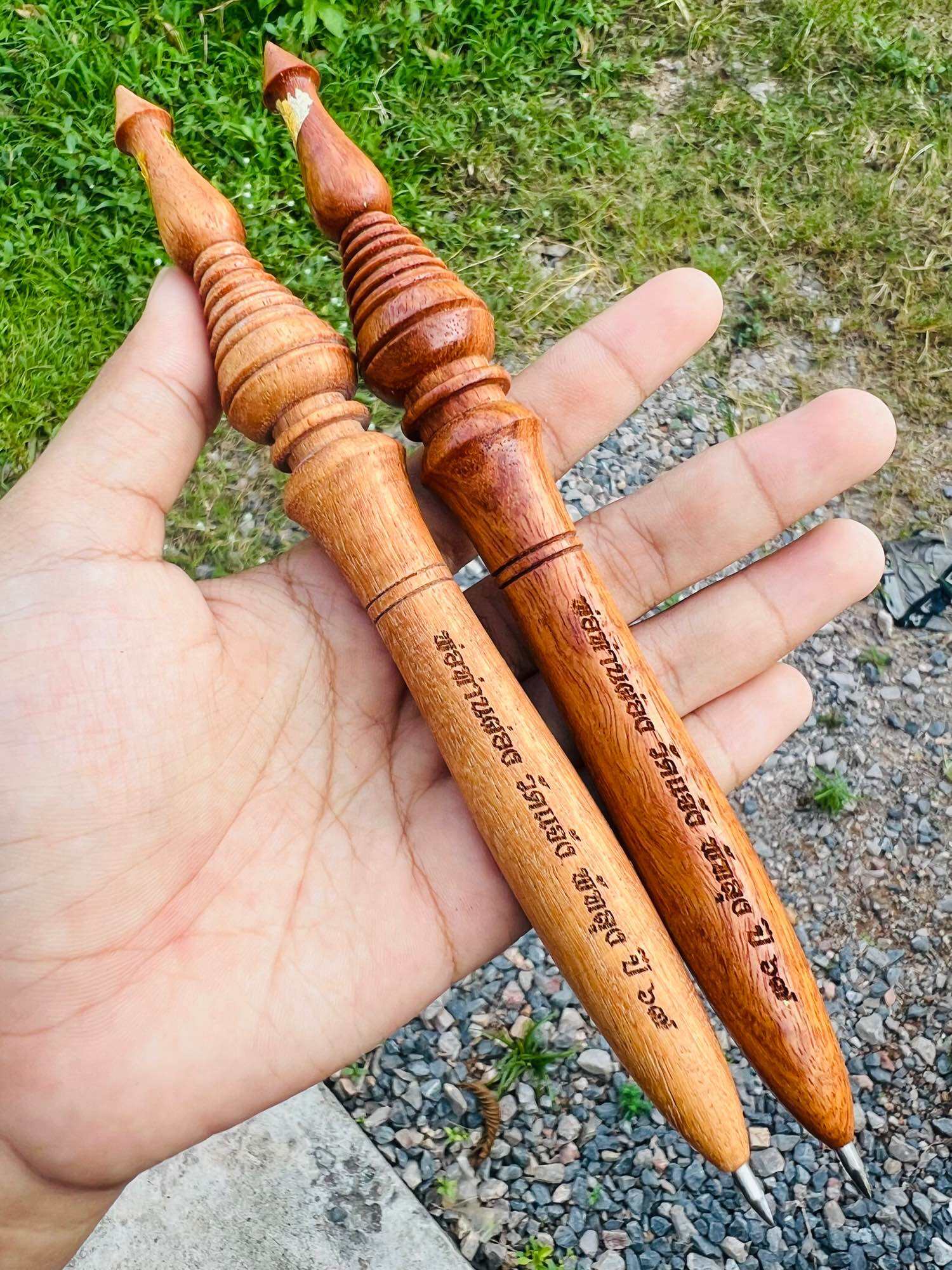 Hand holding two carved wooden Thai spiritual master stick with engraved Thai script and decorative finials