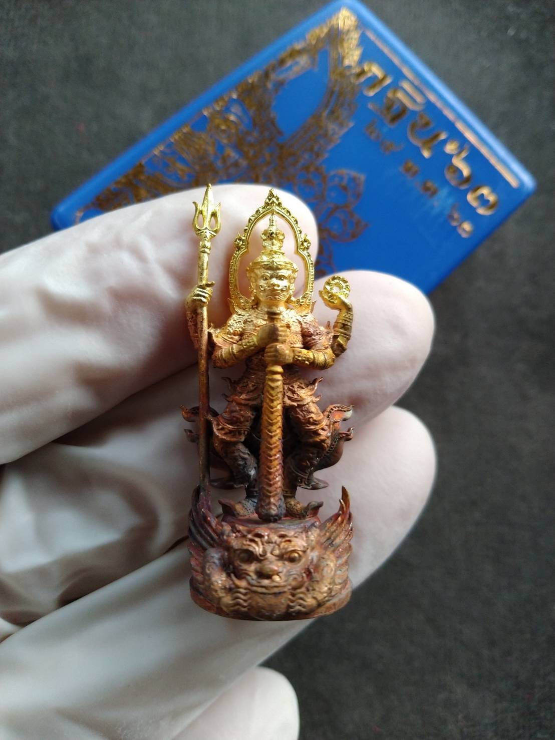 Thao Wessuwan statue for wealth and protection. Thai Blessing Co gold and red amulet pendant held in glove