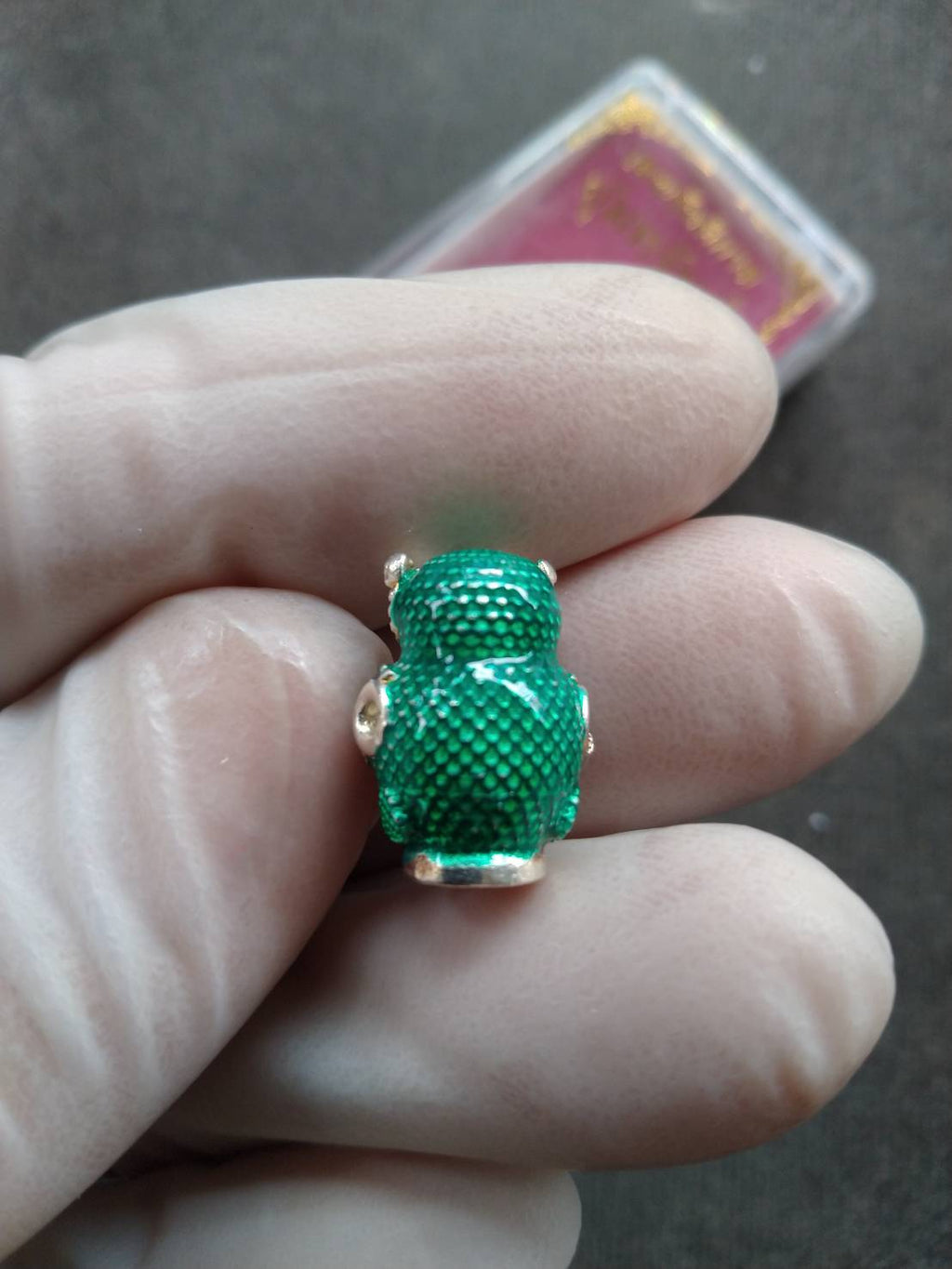 Thai Blessing Co green textured mini amulet pendant featuring Thevarattikan Wealth Embracing Deity held between gloved fingers