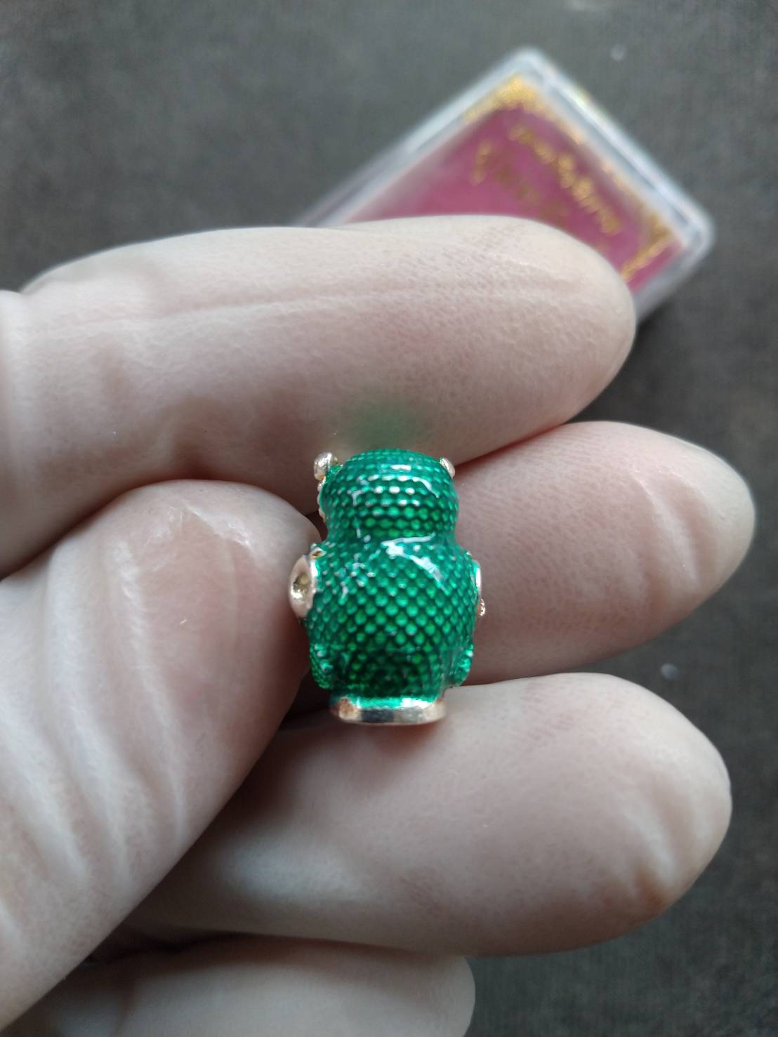 Thai Blessing Co green textured mini amulet pendant featuring Thevarattikan Wealth Embracing Deity held between gloved fingers