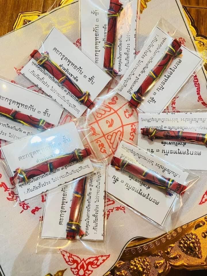 Triple-layer Phuttha Takrud amulet packets arranged in a circle on yantra cloth showing red rolled amulets with labels