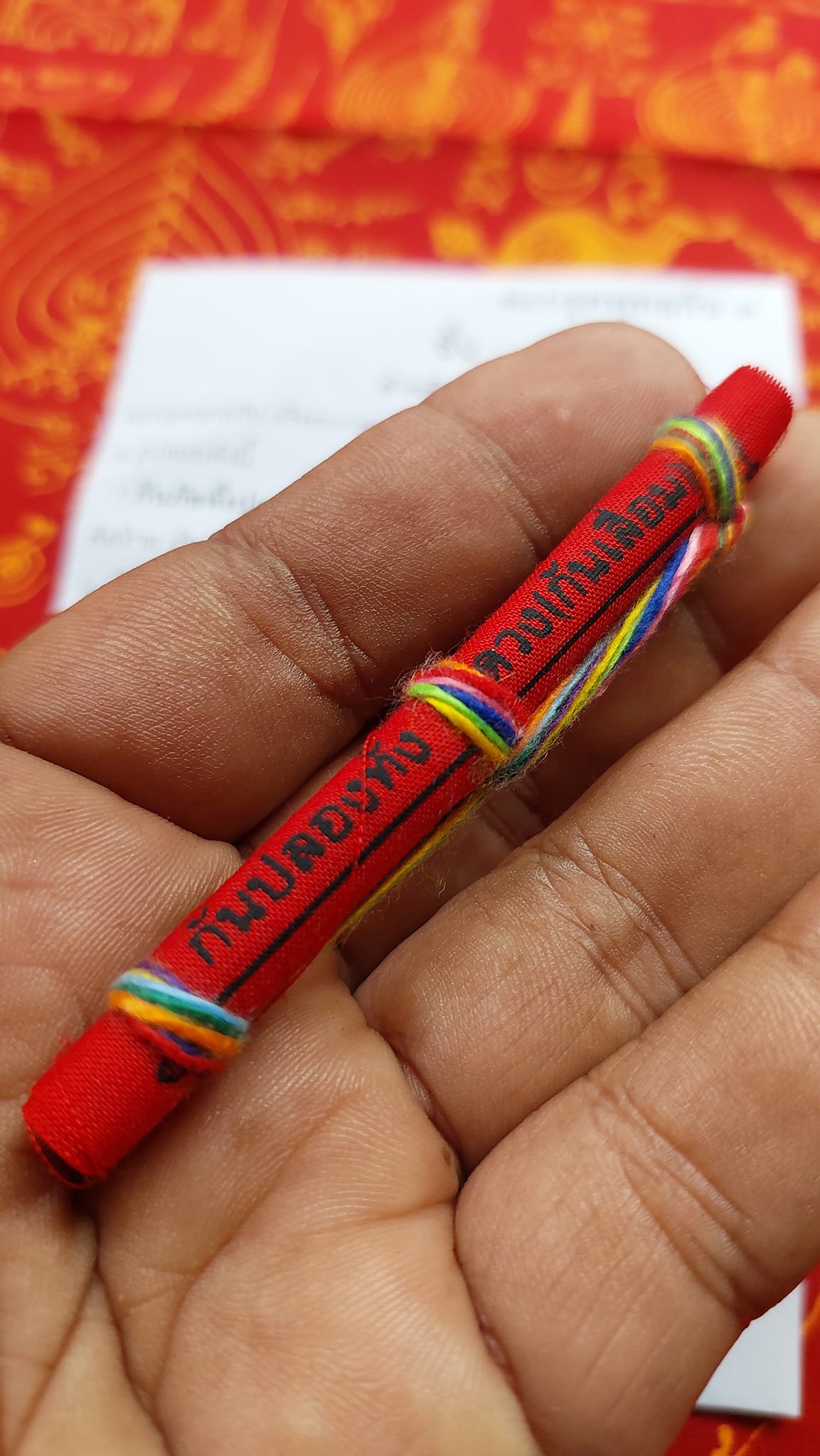 Triple-layer Phuttha Takrud amulet red cloth scroll wrapped in multicolor thread held in hand