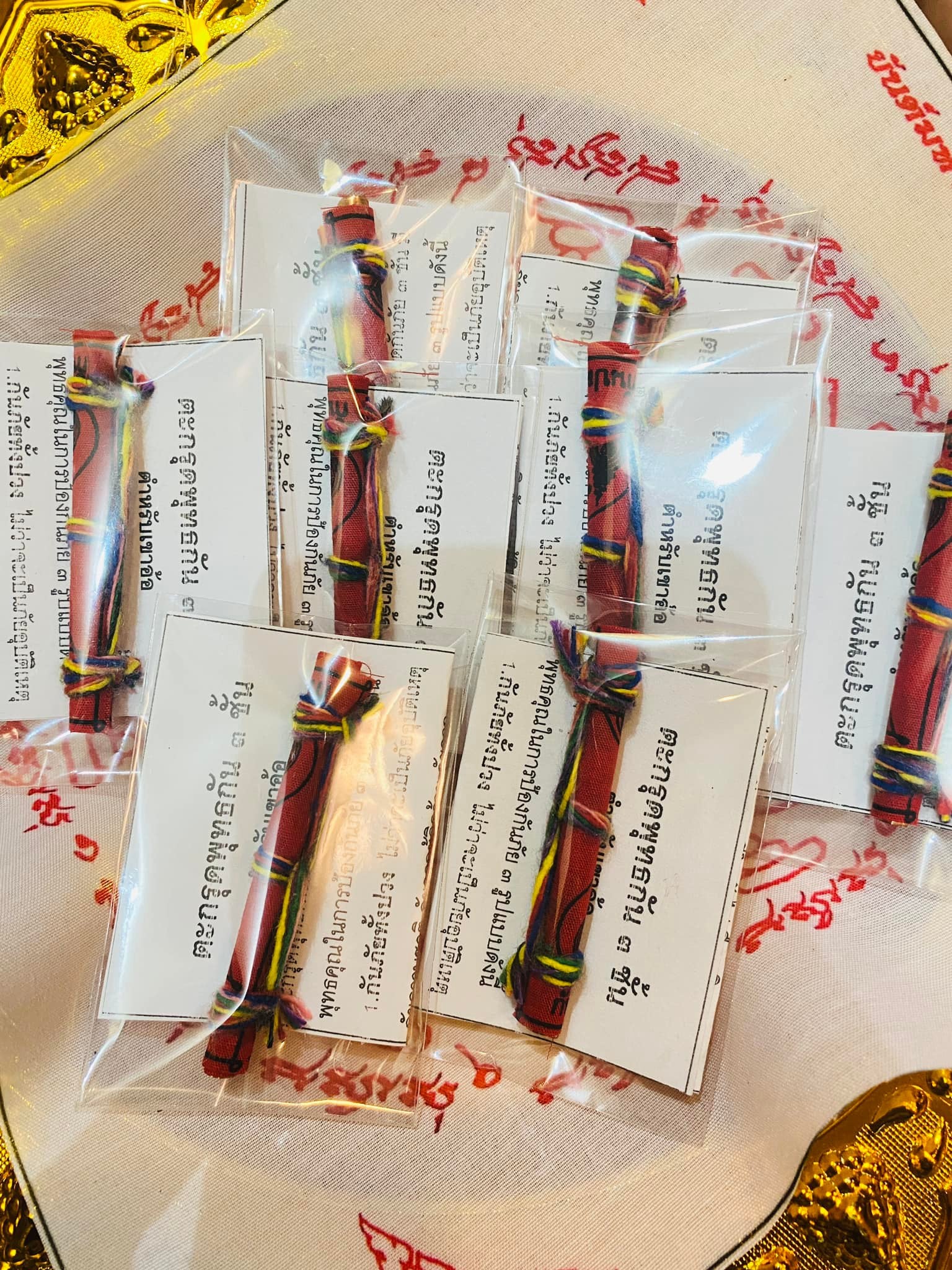 Triple-layer Phuttha Takrud amulet red braided cords with yellow and black threads in clear packaging on ceremonial cloth