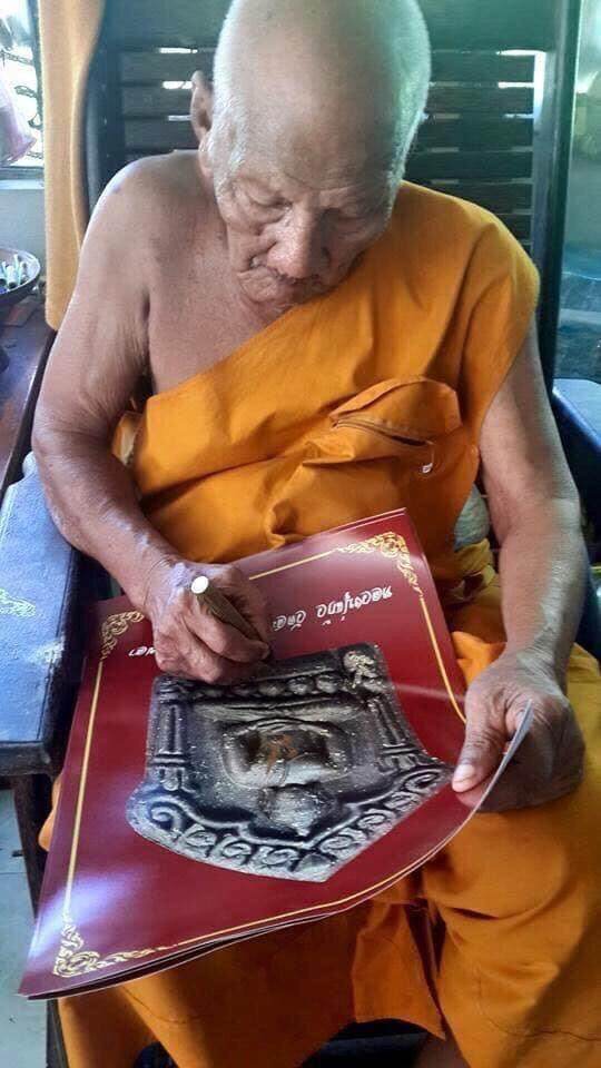 Elder monk in saffron robe signing amulet poster for Phra Khun Paen Amulet - Blessed by Luang Pu Kaew, Wat Sapan Mai Kaen.