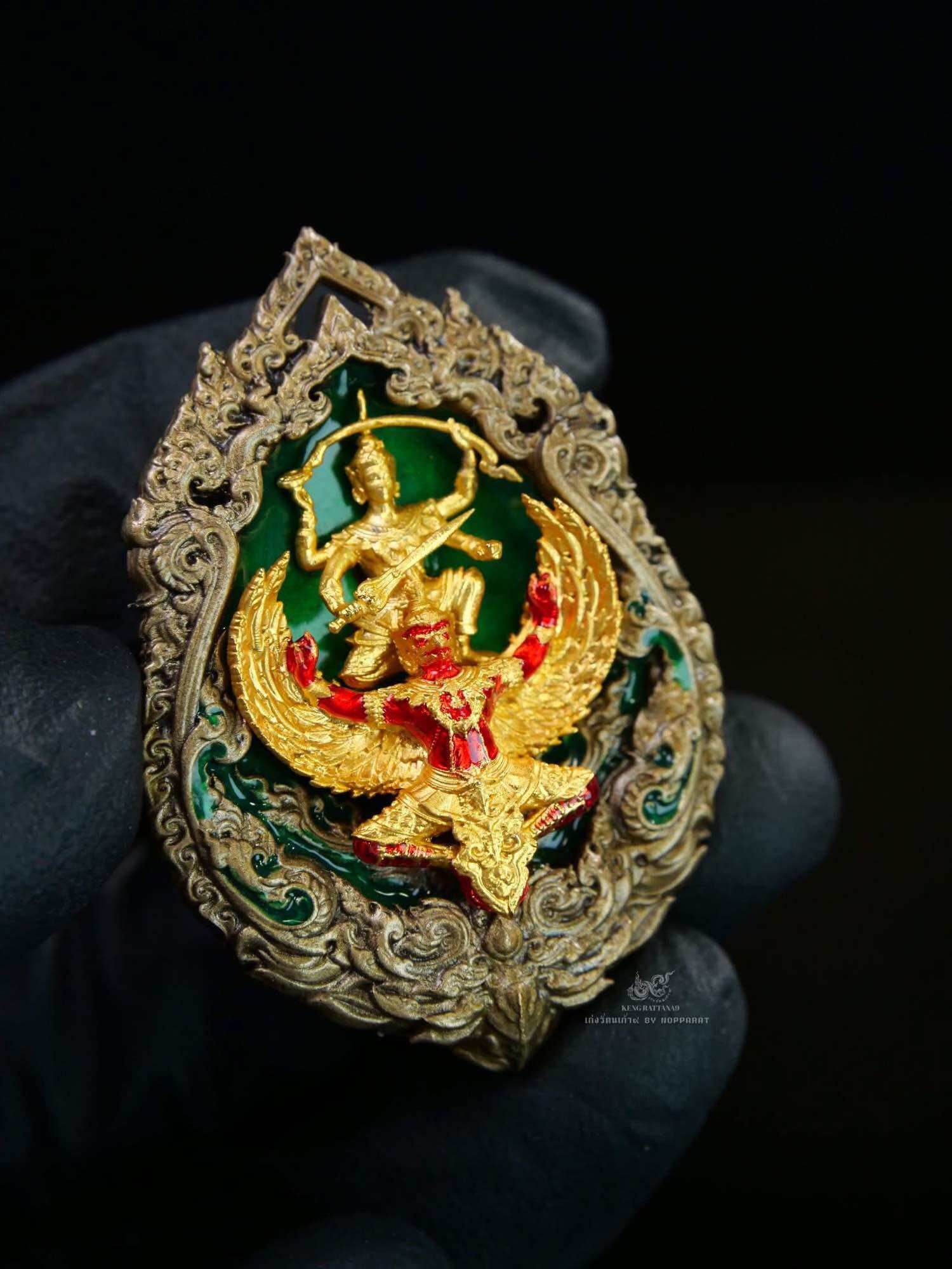 Gold Narayana on Garuda Medallion with green enamel and red accents ornate Thai amulet held in gloved hand