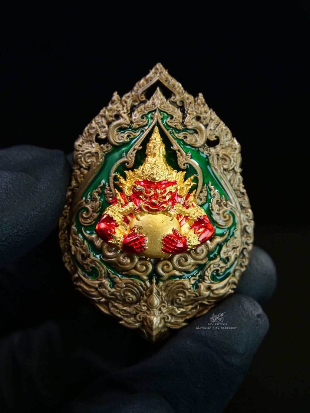 Narayana on Garuda Medallion ornate Thai amulet in gold red and green with detailed filigree held in gloved hand