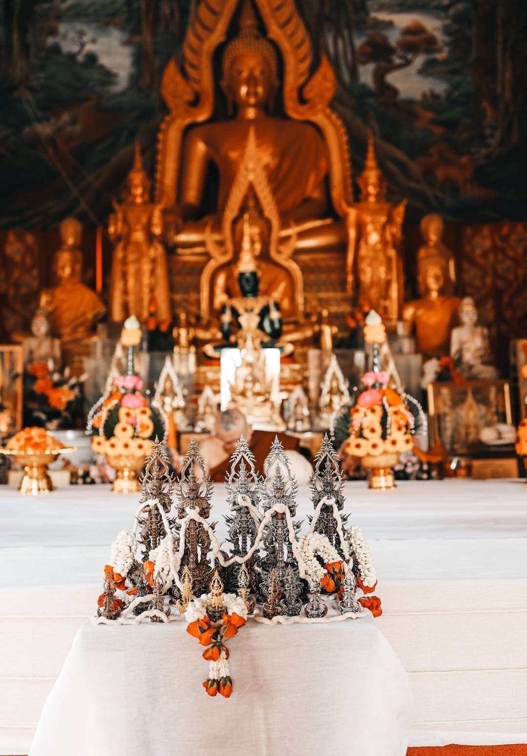 Thao Wessuwan statue for wealth and protection. Ornate Thai amulets on altar table with large Buddha figures in background