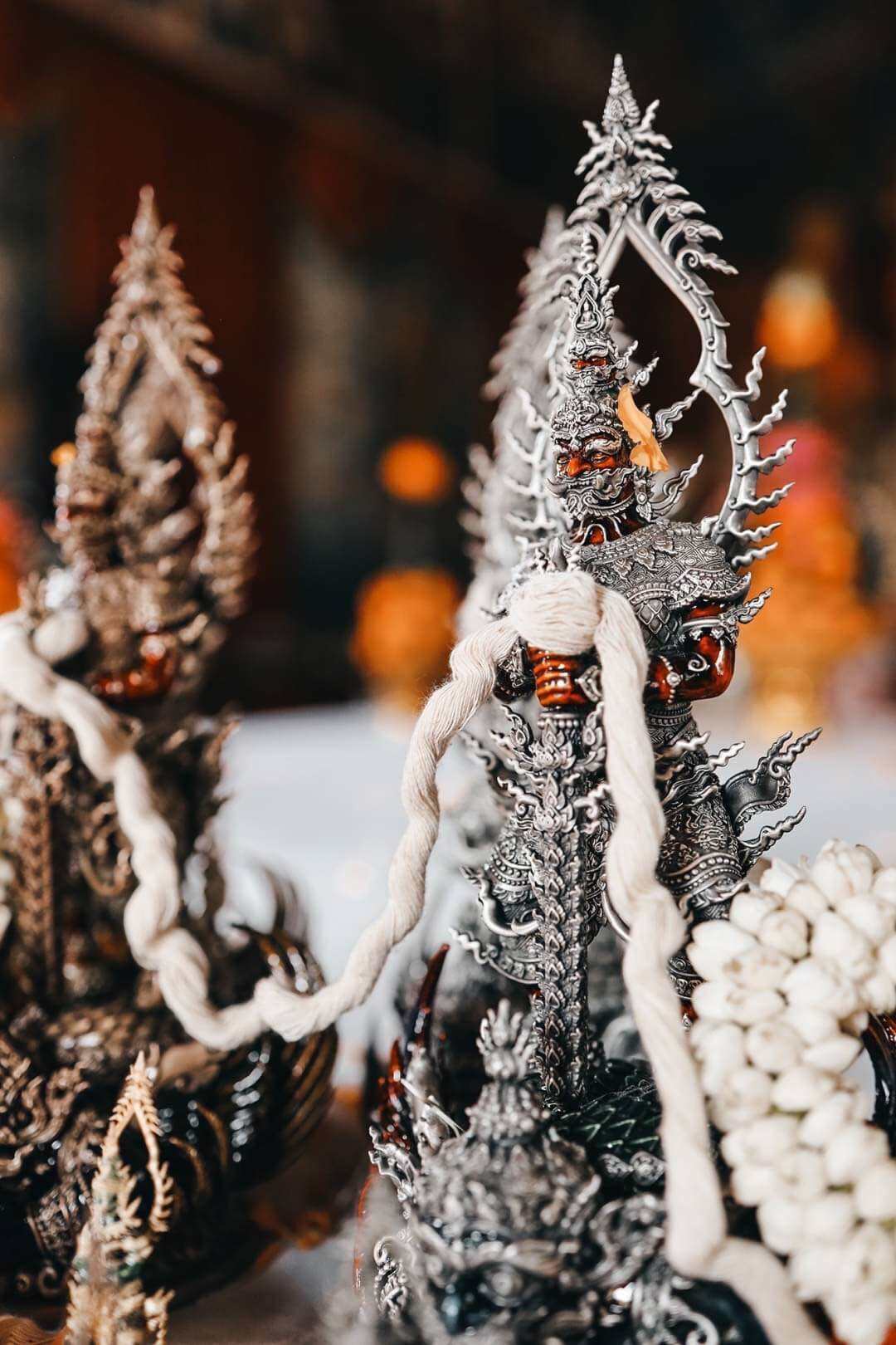 Intricate silver pendant display featuring Thao Wessuwan statue for wealth and protection. White cords and jasmine garland