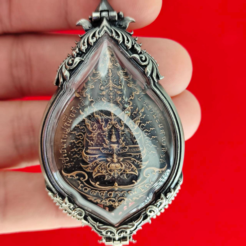Silver teardrop amulet with Thai script and deity carving in resin case Lord Vesuvananno amulet for wealth and protection.